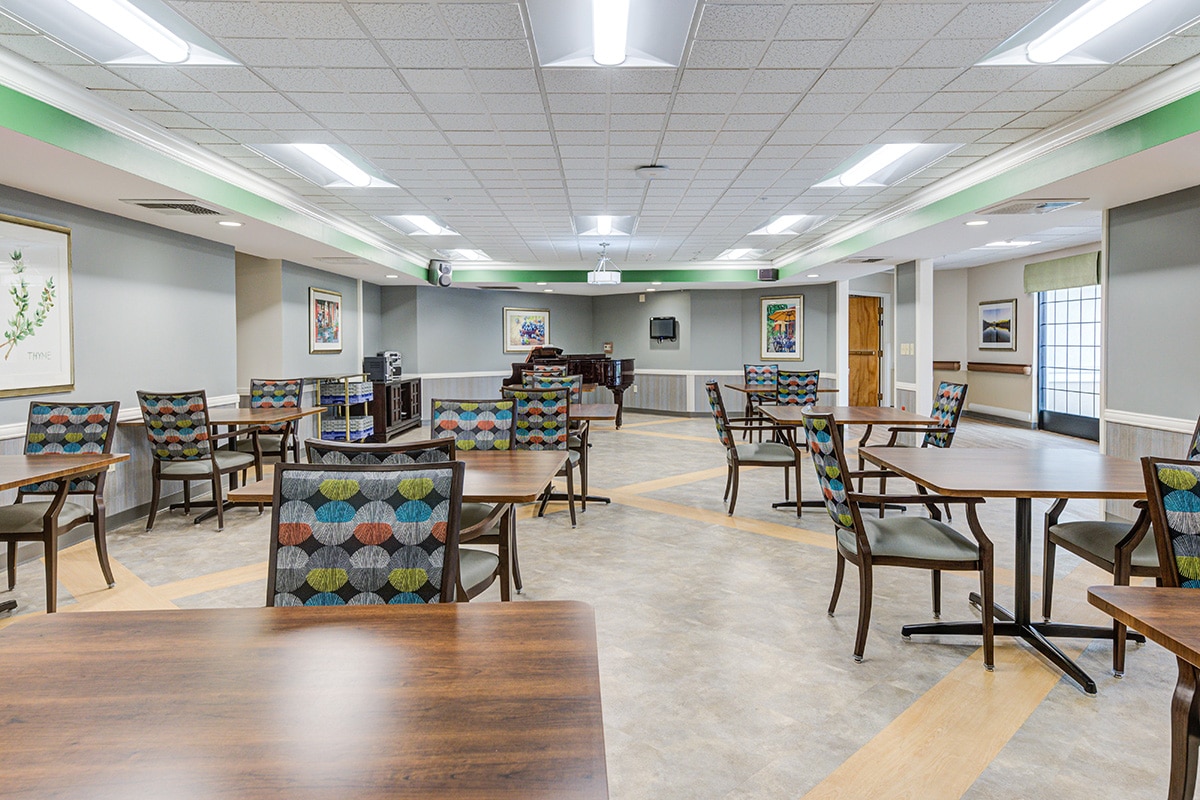 Activity room with many tables and chairs, large windows, and piano.