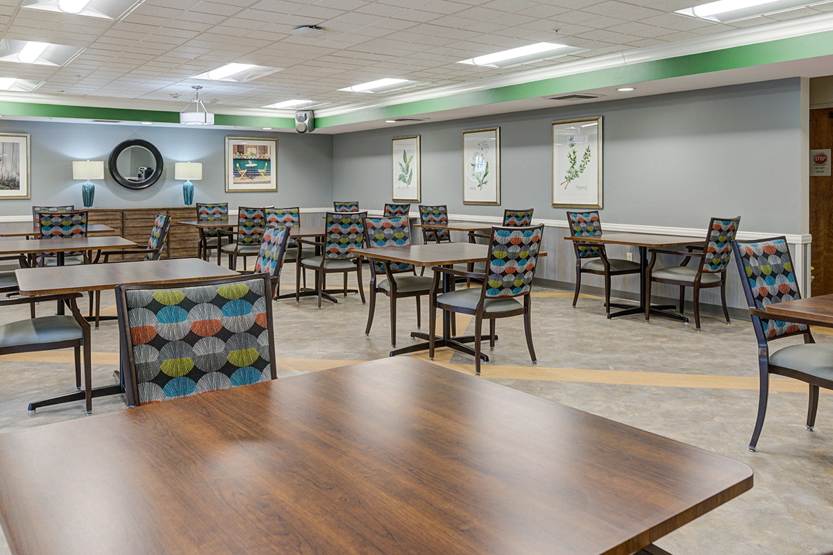Activity/dining room with many tables and chairs and a round mirror on the wall.