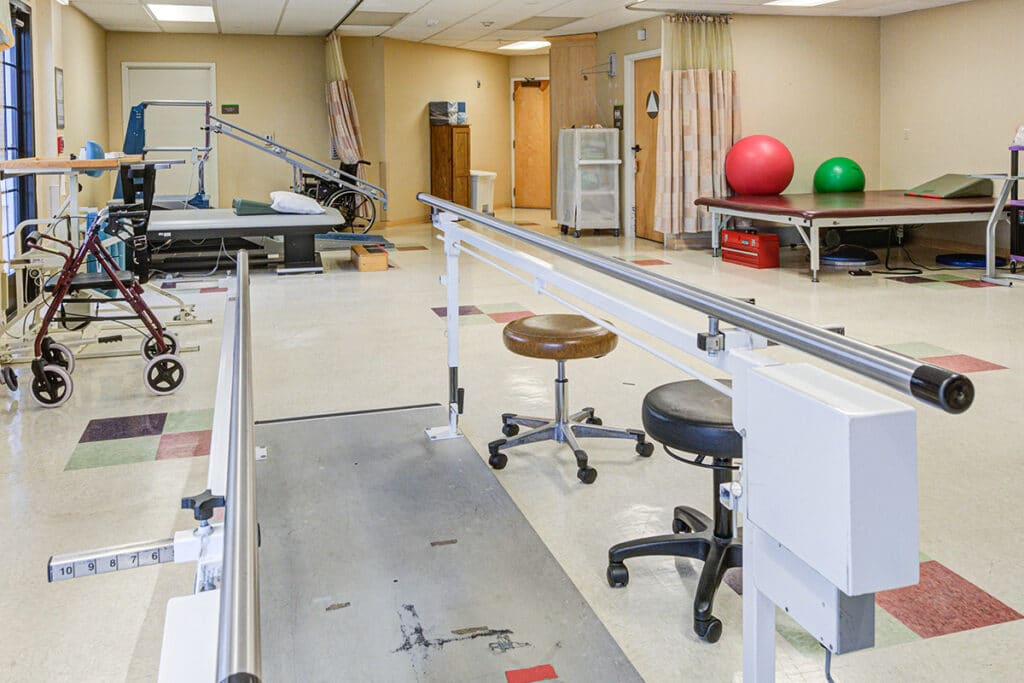 Rehab gym at an angle with parallel bars and other tables and physical therapy equipment.